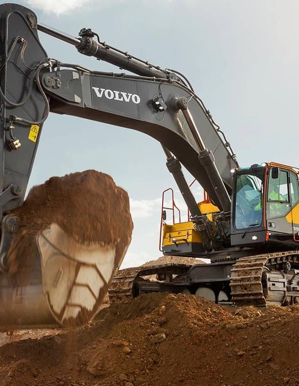 Excavadora hidráulica Volvo de color negro y amarillo con orugas, operando en un terreno de construcción. La cuchara está levantando una gran cantidad de tierra, mostrando su potencia y eficiencia en excavaciones pesadas.